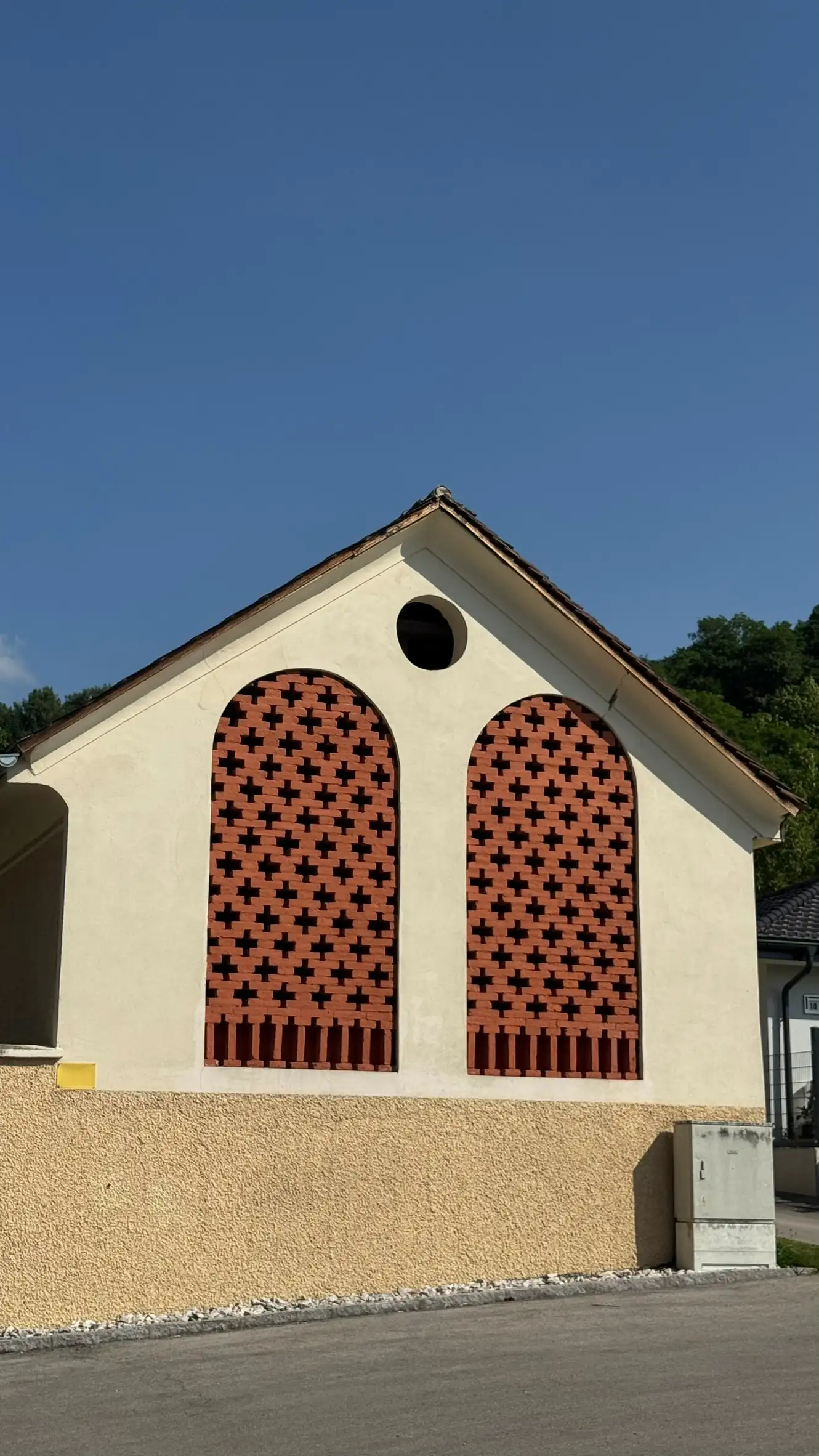 Outbuilding for storage; two tall, arched openings with brick latticework; circular vent