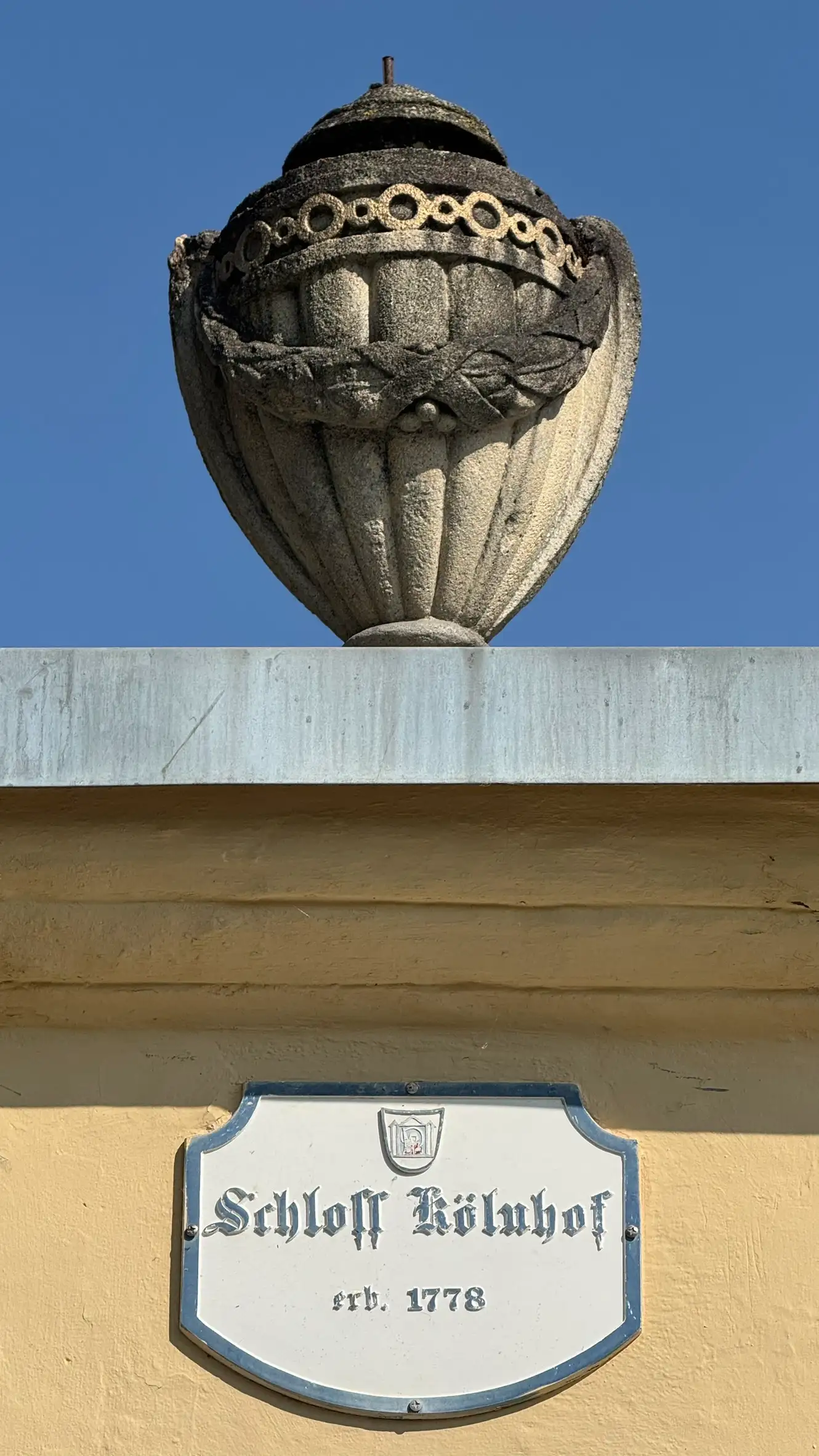 Neoclassical vase on a pillar beside the entrance gate and signage