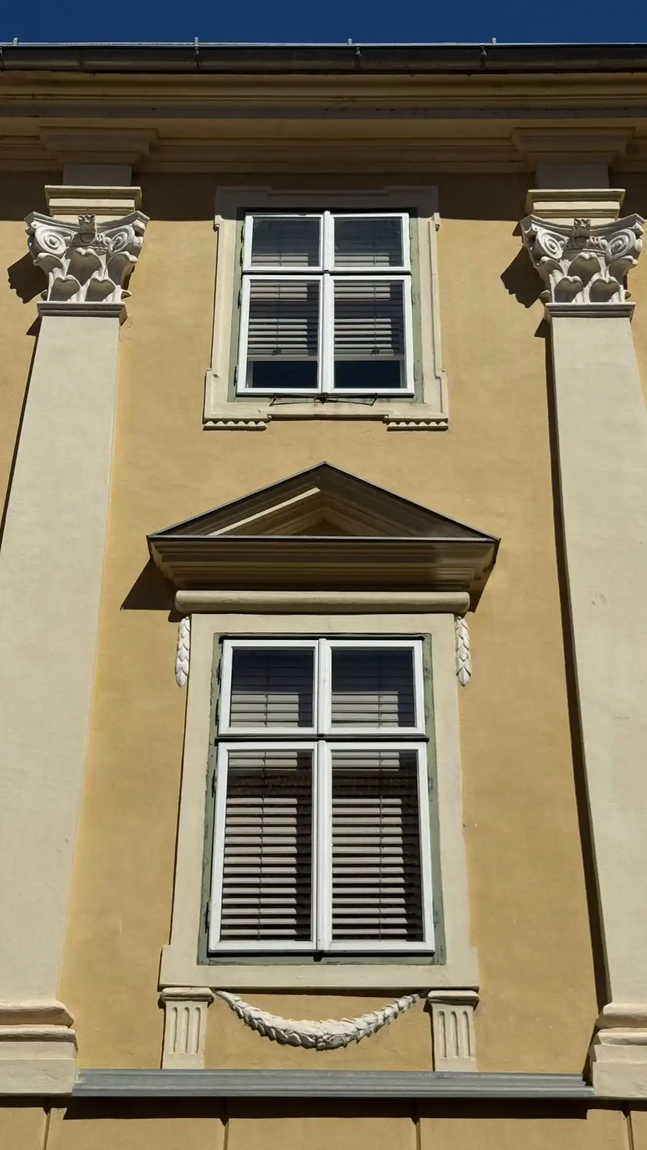 Flanked by pilasters, the lower window features a triangular pediment above and a braid-style (Zopfstil) garland below.
