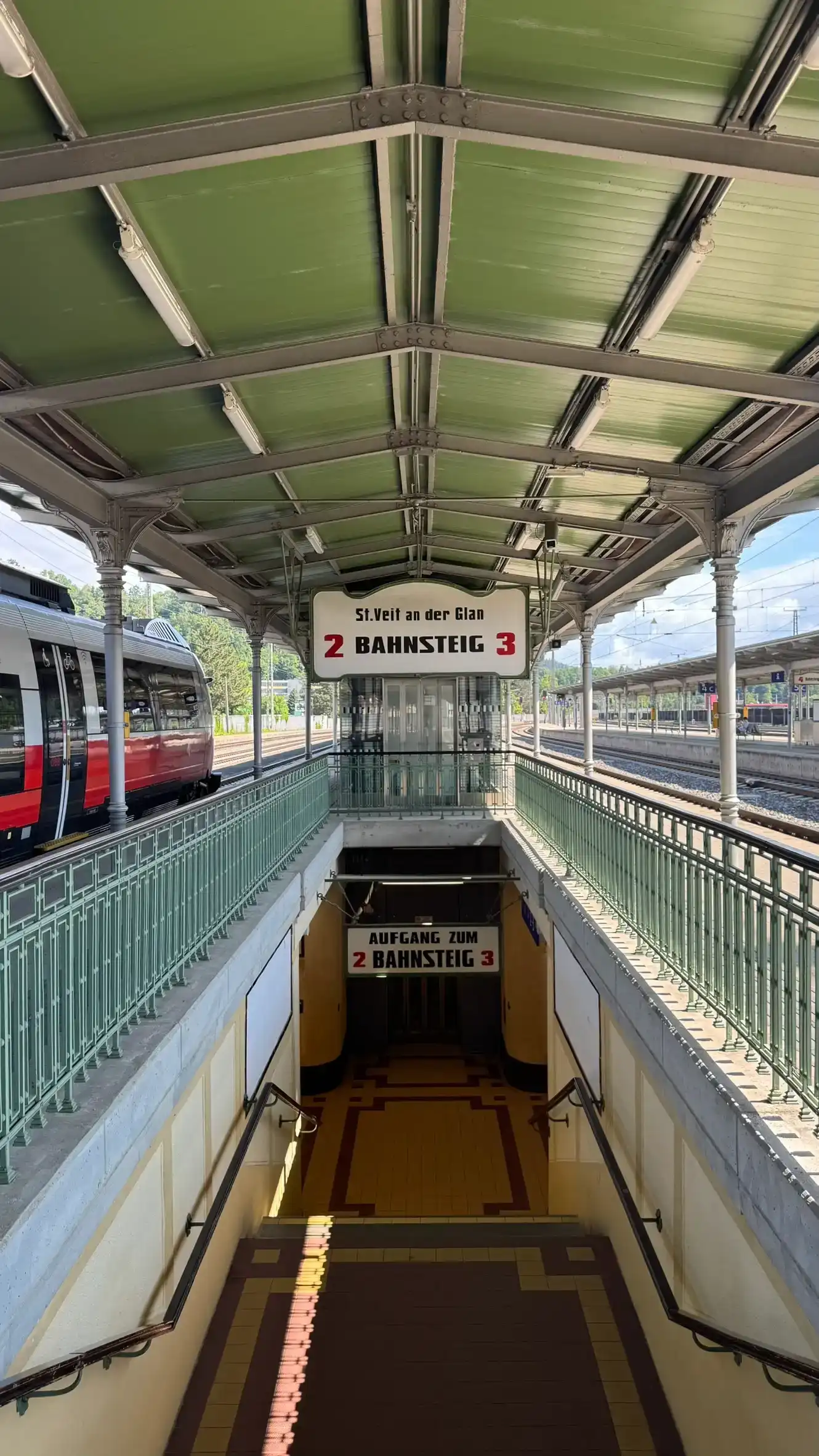 Inselbahnsteig mit in Lindgrün gestrichenem Dach und Geländer, Treppe zur Unterführung sowie historischem Schild für die Bahnsteigkanten 2 und 3