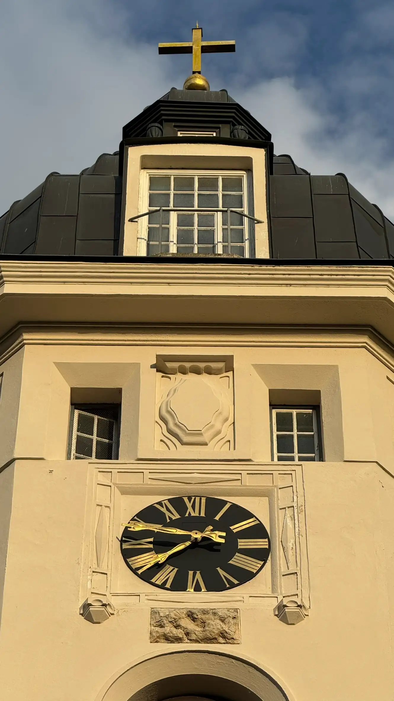 Tower roof with cross finial and frontal window; upper section with two rectangular windows above clock