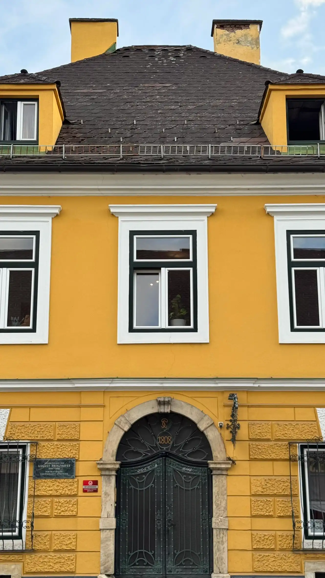 Chimneys, hipped roof with dormer windows, white-framed windows, and wrought-iron double-leaf door with round stone arch