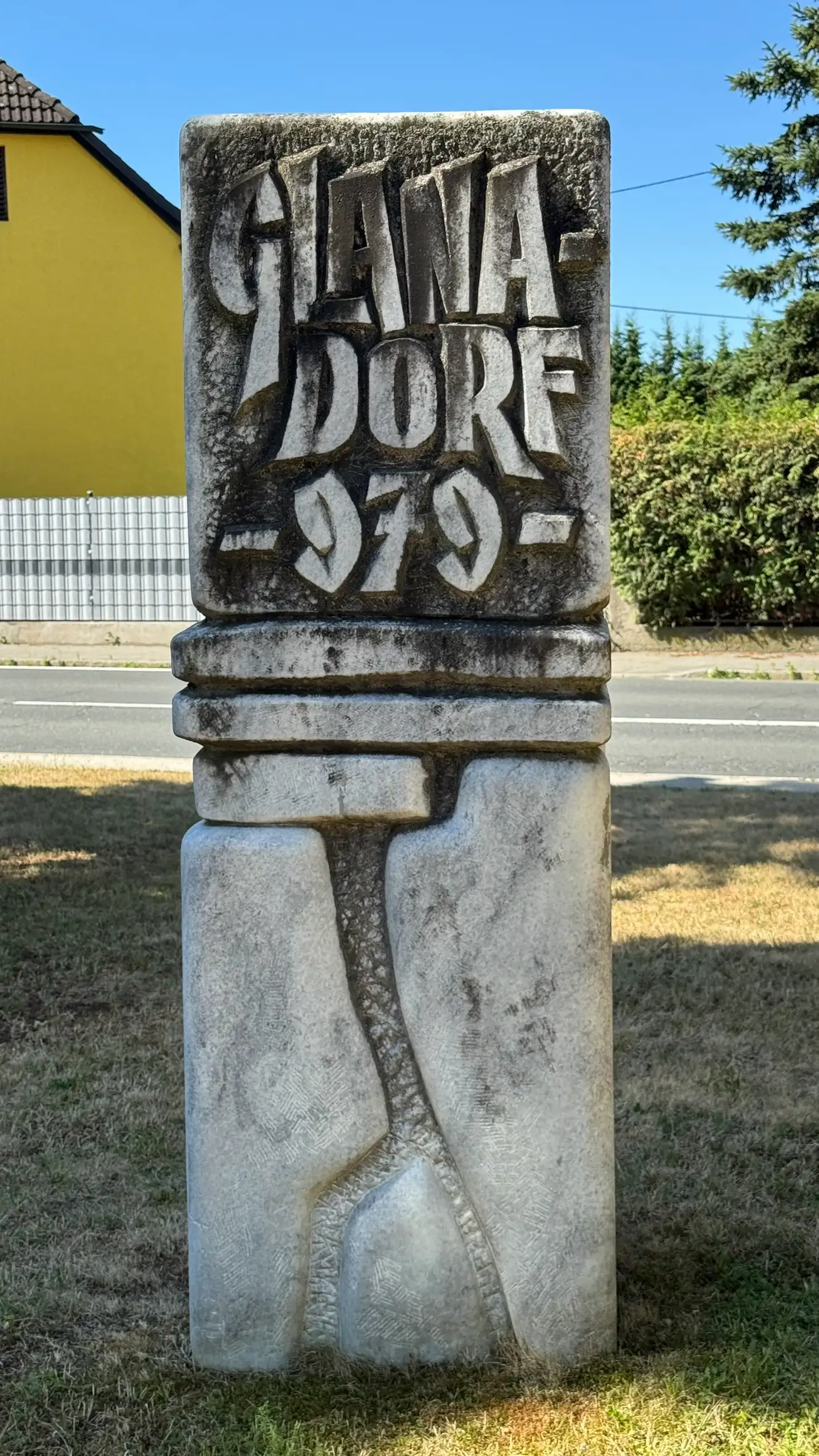 Unterer Abschnitt: kubischer Sockel; mittlerer Abschnitt: gestaltete Platten; oberer Abschnitt: reliefierte Inschrift „Galanadorf 979“