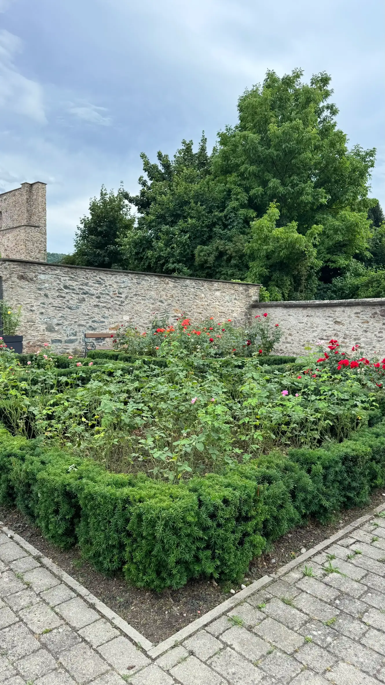 Vordergrund: Weg mit rechteckigen Steinplatten und Blumenbeeten.