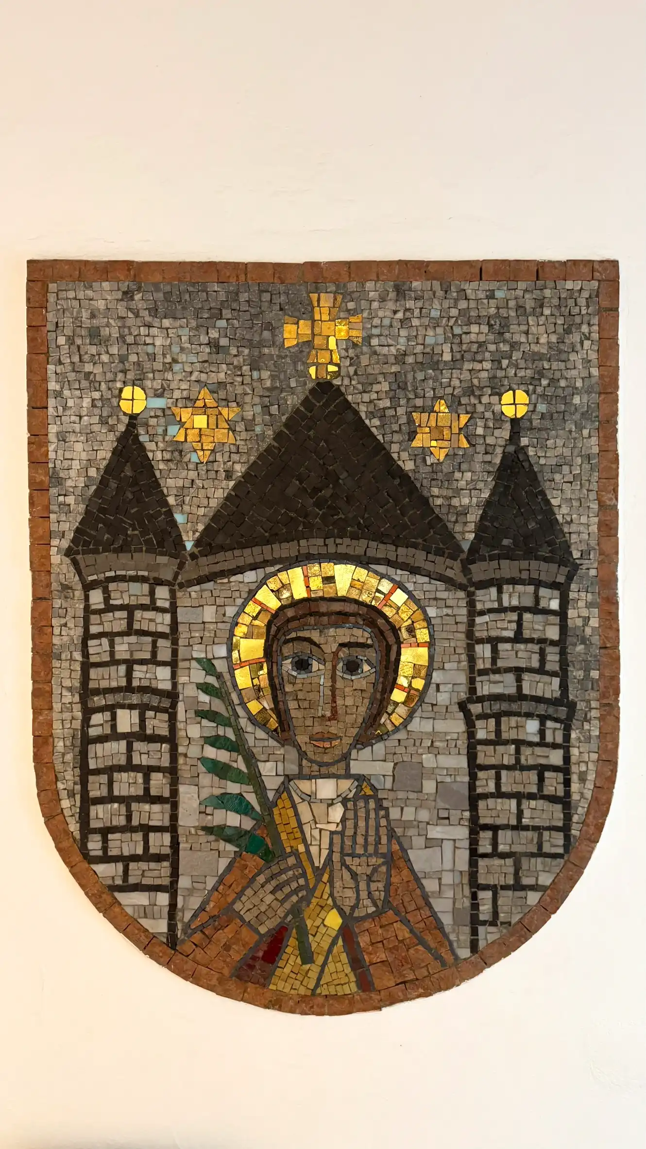 Der Heilige ist frontal dargestellt, gerahmt von der stilisierten Architektur eines befestigten Tores mit zwei Türmen und einem mittleren Dach.