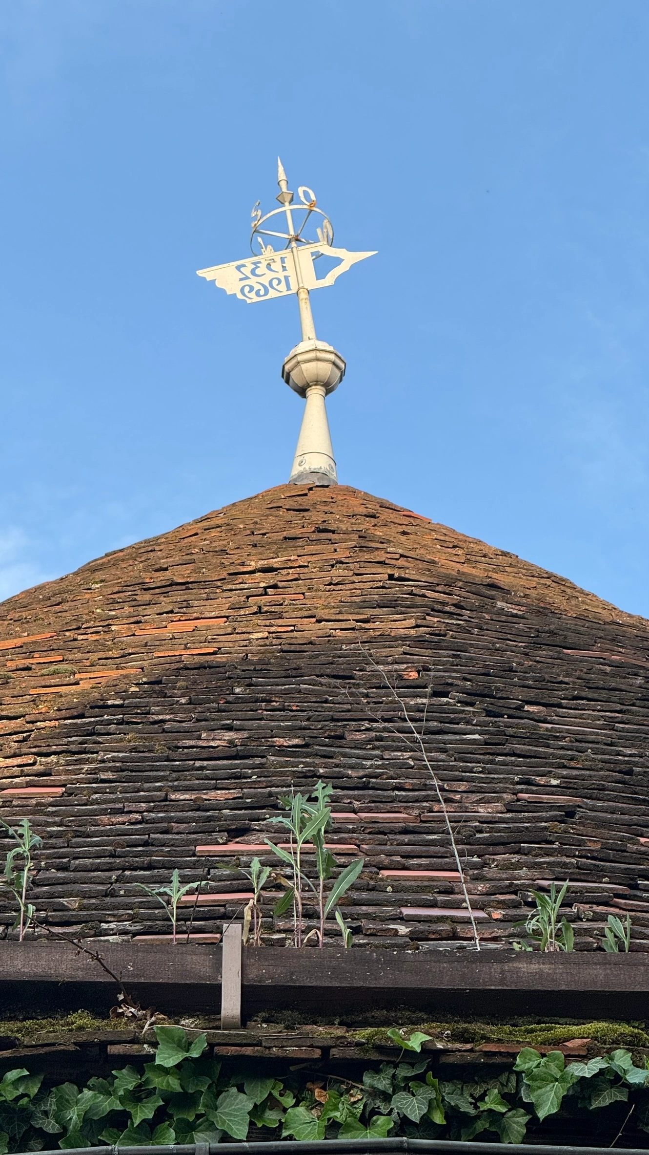Tiled conical roof with knobbed finial and weathervane, dated 1555.