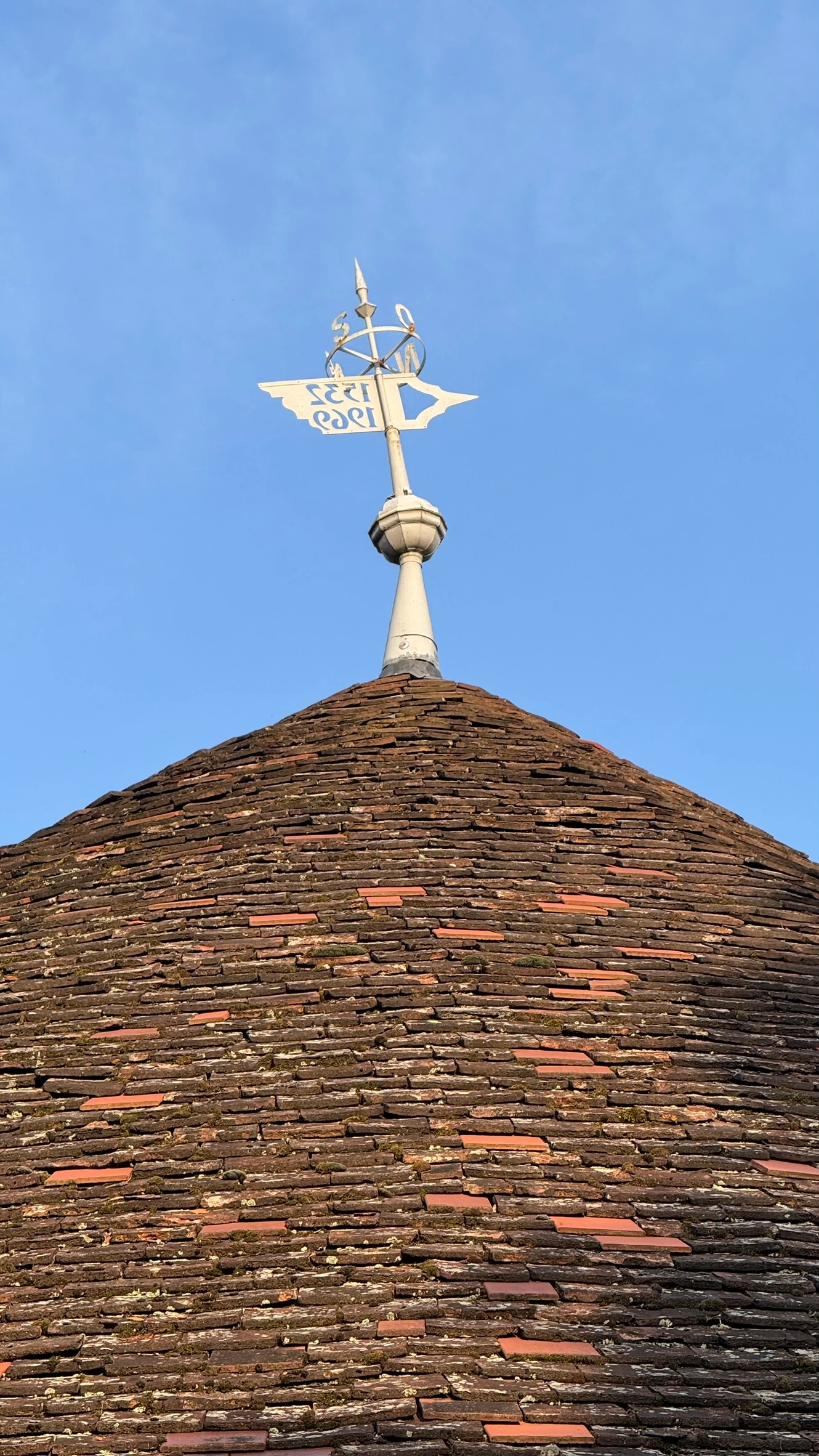 Close-up of the tiled conical roof with knobbed finial and weathervane, dated 1555.